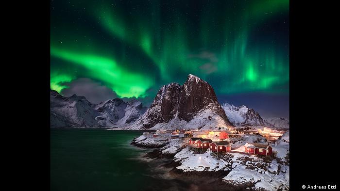 Vivid green Northern Lights shine above a small snowy town with red buildings (Photo: Andreas Ettl ).
